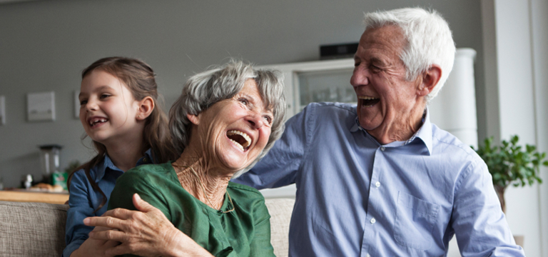 elderly couple laughing on a sofa with grandchild