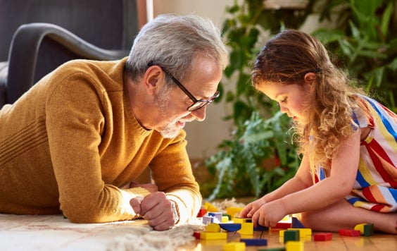 Granddaughter playing with wooden block and granddad watching