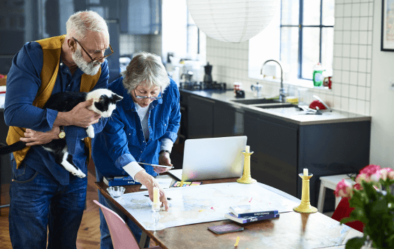 Older man holding cat, whilst his partner points at a map on their dining table