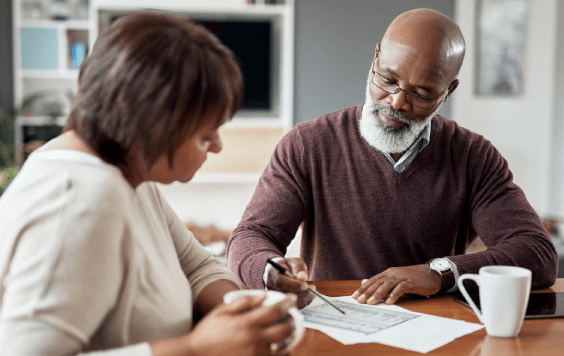 Older adult man and woman, at home, sat at a table looking at detailed papers